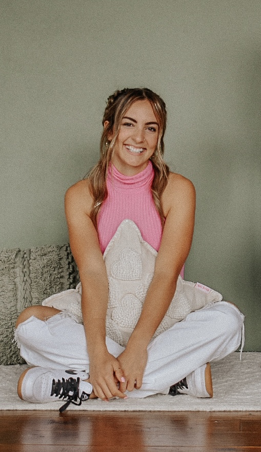 Emmily smiling, sitting cross-legged in a pink top